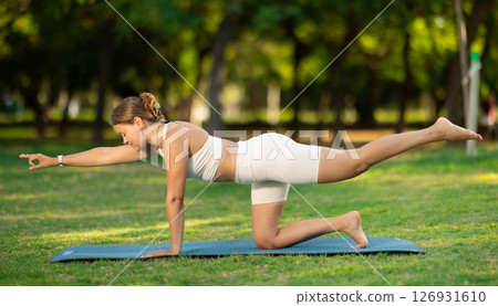 Fit girl performing balancing table yoga pose on green meadow 126931610