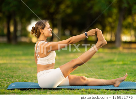 Girl in park on green grass of lawn performs eka padahastasana salamba navasana 126931776