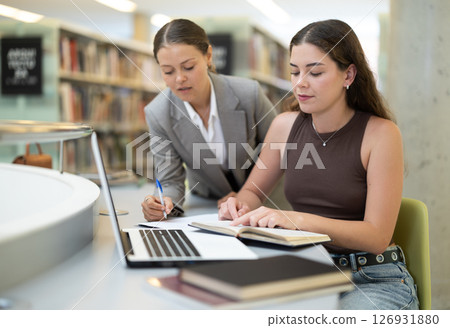 female student works at a notebook, and a fellow student helps her 126931880
