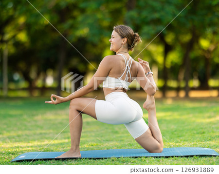 Young yogini performing Crescent Low Lunge Pose in summer park Young yogini performing Crescent Low Lunge Pose in summer park 126931889