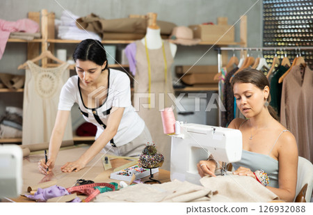 Young seamstresses stitching and drafting paper patterns in workshop Young seamstresses stitching and drafting paper patterns in workshop 126932088