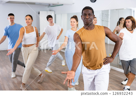 African american man practicing active dance moves during rehearsal with group in dancing studio. African american man practicing active dance moves during rehearsal with group in dancing studio. 126932243