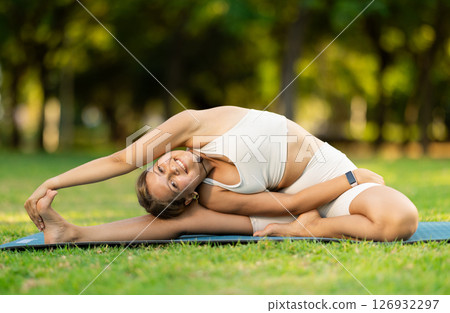 Girl in park on green grass of lawn performs Parivritta Janu Shirshasana 126932297
