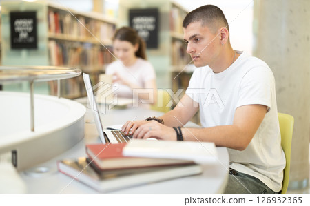 guy with books works in a library against the background of students guy with books works in a library against the background of students 126932365