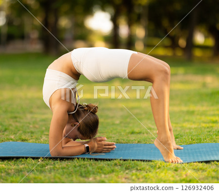 Girl in park on green grass of lawn performs Ardha chakrasana 126932406