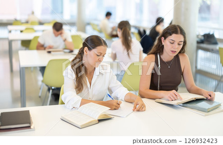 Two female student friends studying for exams together in university library 126932423