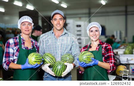Smiling factory workers holding ripe whole watermelons and looking at camera during sorting ripe watermelons on conveyor 126932432