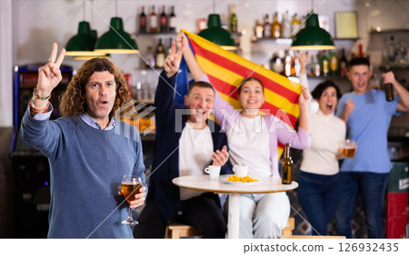 Excited sports supporters of different ages with flag of Estelada, rejoicing winning game with beer and snacks in pub 126932435