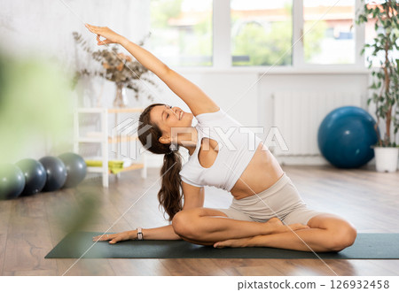 Woman sitting on a sports mat doing stretching during yoga classes Woman sitting on a sports mat doing stretching during yoga classes 126932458