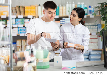 Young man with prescription is shopping in pharmacy, pharmacist offer remedy for treatment Young man with prescription is shopping in pharmacy, pharmacist offer remedy for treatment 126932459