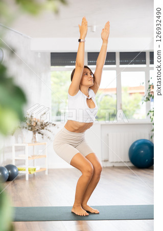 Experienced girl fitness club teacher performs chair asana, utkasana Experienced girl fitness club teacher performs chair asana, utkasana 126932490