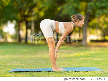 Girl in park on green grass of lawn performs Uttanasana 126932511