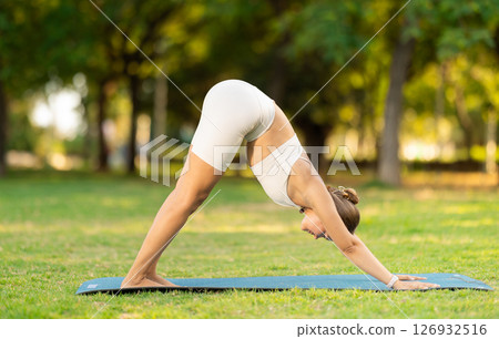 Young woman doing Downward Facing Dog Pose in summer park 126932516