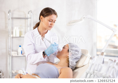 Aesthetician administering hardware facial procedure with ice hammer on young woman Aesthetician administering hardware facial procedure with ice hammer on young woman 126932524