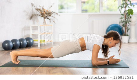 Young woman yoga trainer performing plank pose on black rug Young woman yoga trainer performing plank pose on black rug 126932581