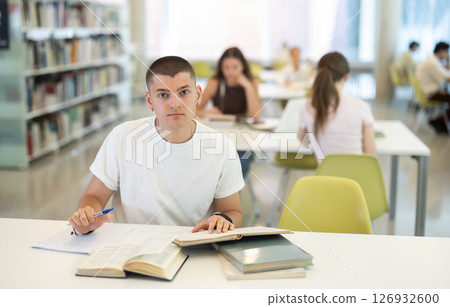 guy is sitting at the table, reading a book and taking notes 126932600