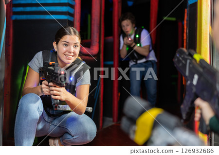 Smiling girl with laser pistol during playing laser tag with her friends in room Smiling girl with laser pistol during playing laser tag with her friends in room 126932686