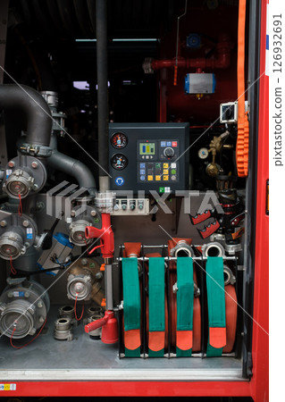 Equipment used for firefighting is neatly organized in a fire truck compartment with hoses, valves, and control panels present in the background during daylight hours Equipment used for firefighting is neatly organized in a fire truck compartment with hoses, valves, and control panels present in the background during daylight hours 126932691