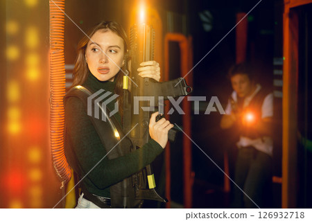Joyous girl with laser pistol playing laser tag with friends on labyrinth Joyous girl with laser pistol playing laser tag with friends on labyrinth 126932718