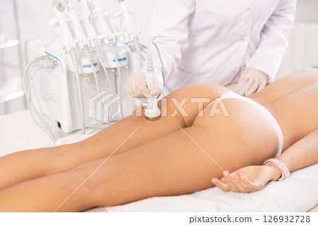 Aesthetician administering high frequency ultrasound procedure on buttocks of female patient 126932728