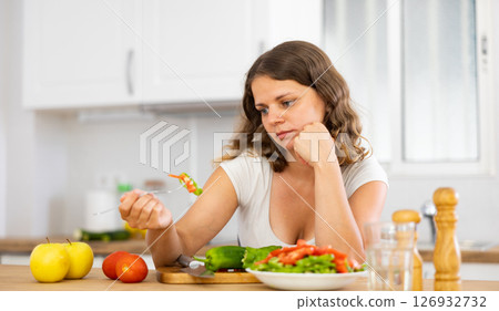 Sad woman eating vegetable salad in kitchen 126932732