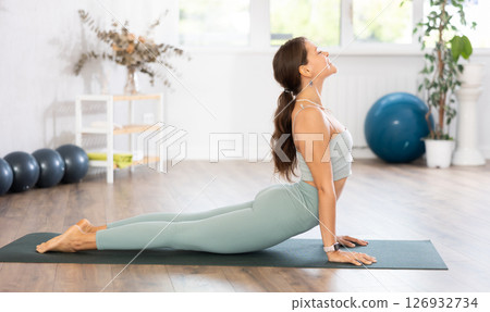 Young woman yoga trainer performing cobra pose on black rug Young woman yoga trainer performing cobra pose on black rug 126932734