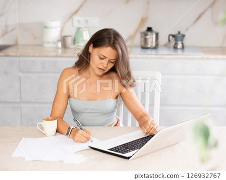 Young woman working on laptop in kitchen 126932767