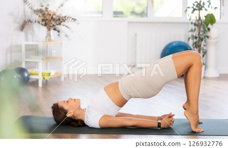 Young woman yoga trainer performing bridge pose on black rug 126932776