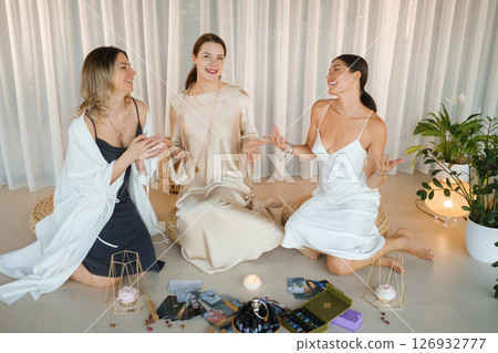 Three girls in dresses sitting on the floor doing a hands-on activity on health, beauty and creativity. Three beautiful girls chatting indoors Three girls in dresses sitting on the floor doing a hands-on activity on health, beauty and creativity. Three beautiful girls chatting indoors 126932777
