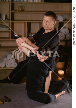 Client in Thai massage session with therapist. A man giving a Thai neck massage to a girl in a spa salon Client in Thai massage session with therapist. A man giving a Thai neck massage to a girl in a spa salon 126932815