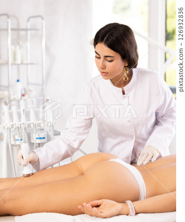 Cosmetologist performing ultrasound liposuction on posterior thighs of female client 126932836