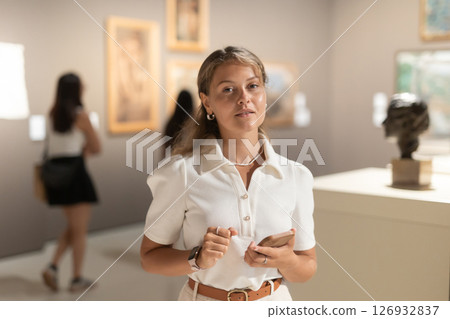 Girl with phone in hands walks around museum hall, view exhibition items Girl with phone in hands walks around museum hall, view exhibition items 126932837