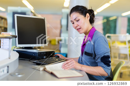Woman engaged in self-education using pc for searching information in libraryary Woman engaged in self-education using pc for searching information in libraryary 126932869