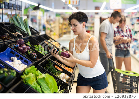 Latin american young female shopper choosing eggplants in store 126932870