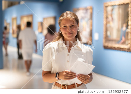 Woman with sheet piece of paper in hands view pictures and icons in museum hall Woman with sheet piece of paper in hands view pictures and icons in museum hall 126932877