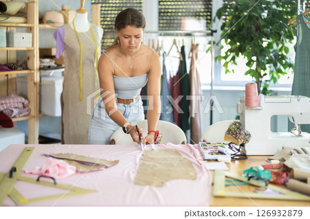 Female fashion designer cutting fabric along pinned paper patterns 126932879