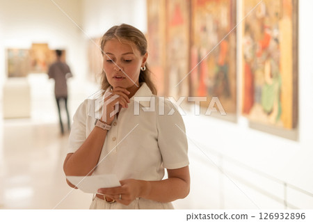 Girl reads an information booklet while visiting gallery of paintings and drawings at an exhibition in museum 126932896