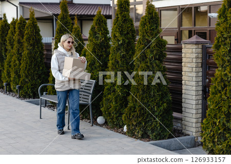 Woman carrying cardboard boxes while walking in residential area 126933157