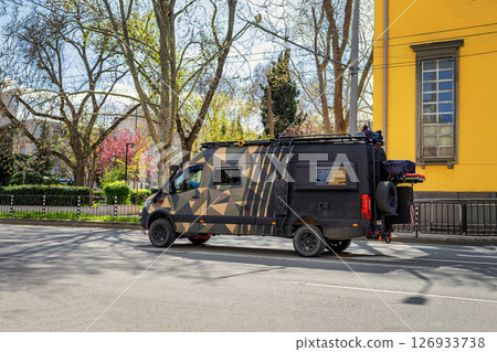 Camper, camouflage van going into nature for adventure, freedom. Modern camper van with geometric camouflage design leaving city streets for nature on spring day. Concept of travel, adventure Camper, camouflage van going into nature for adventure, freedom. Modern camper van with geometric camouflage design leaving city streets for nature on spring day. Concept of travel, adventure 126933738