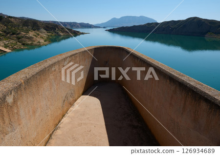 Concrete Balcony Overlooking Calm Lake and Scenic Mountain Views Under Clear Blue Sky 126934689