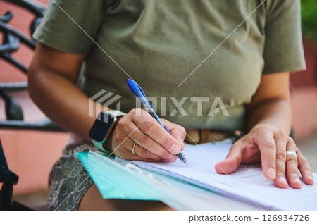Close-Up of a Person Writing with a Pen on Documents Outdoors 126934726