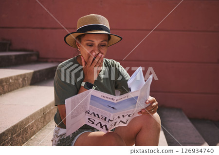 Woman Reacting Emotionally While Reading Surprising News in a Newspaper and Sitting Outdoors Woman Reacting Emotionally While Reading Surprising News in a Newspaper and Sitting Outdoors 126934740