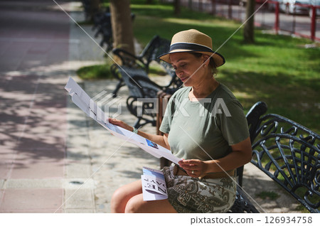 Woman Sitting on a Bench in a Park Reading a Newspaper Outdoors 126934758