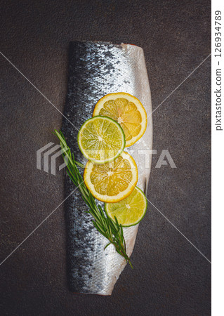 Fresh fish fillet, garnished with lemon and herbs, on a dark background, ready to cook Fresh fish fillet, garnished with lemon and herbs, on a dark background, ready to cook 126934789