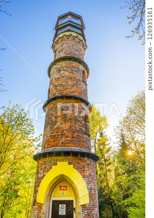 The Kopanina Lookout Tower stands tall in the lush greenery of Bohemian Paradise, offering visitors scenic views and a charming historical experience on a sunny day in Czechia. The Kopanina Lookout Tower stands tall in the lush greenery of Bohemian Paradise, offering visitors scenic views and a charming historical experience on a sunny day in Czechia. 126935161