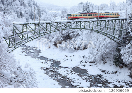 The Toyama Chiho Railway slowly crosses the Chigasaki iron bridge over the frozen Jōganji River. 126936069