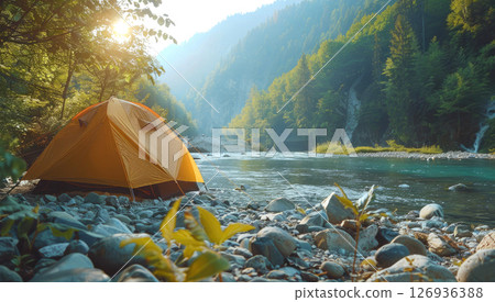 Orange tourist tent is set up on the rocky bank of a mountain river in the forest, on a sunny day. Concept of hiking, recreation in the wild. 126936388