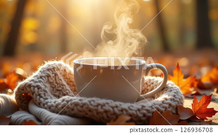 Cup of steaming tea with knitted scarf and autumn leaves, creating a cozy and warm fall atmosphere. 126936708