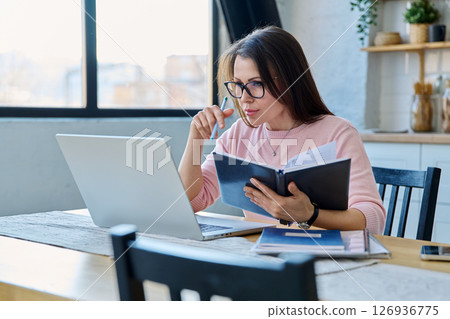 Middle-aged serious woman working at computer laptop in home office Middle-aged serious woman working at computer laptop in home office 126936775