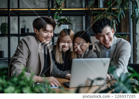 Happy business team collaborating in modern office, laughing and working together with laptops and documents on the desk. 126937285